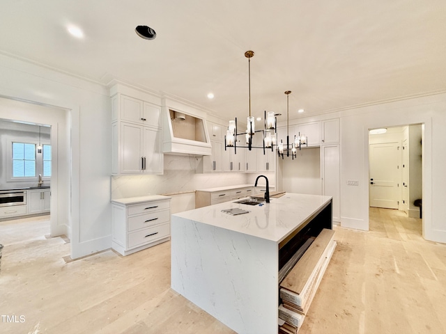 kitchen featuring pendant lighting, sink, light stone countertops, white cabinets, and a center island with sink