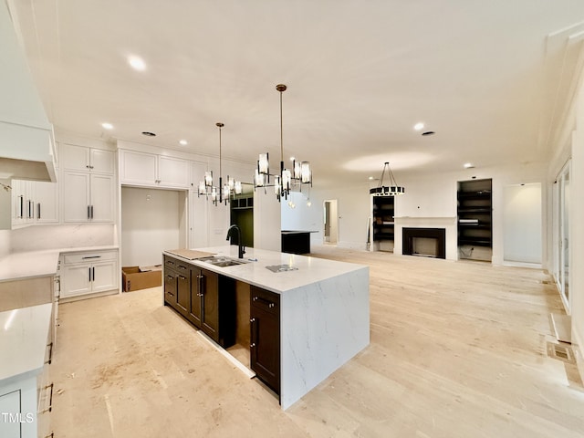 kitchen featuring sink, a center island with sink, white cabinets, and light stone counters