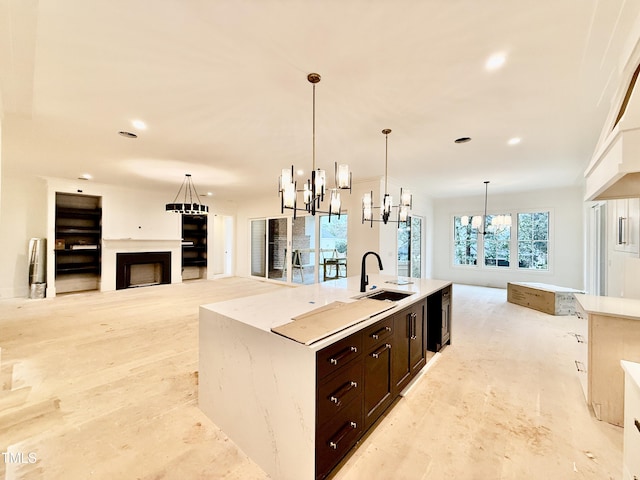 kitchen featuring sink, dark brown cabinetry, light stone countertops, a center island with sink, and decorative light fixtures