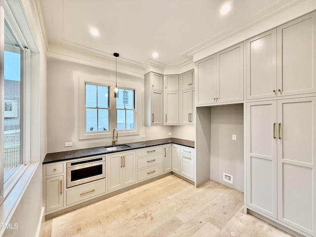 kitchen featuring sink, crown molding, light hardwood / wood-style flooring, stainless steel microwave, and pendant lighting