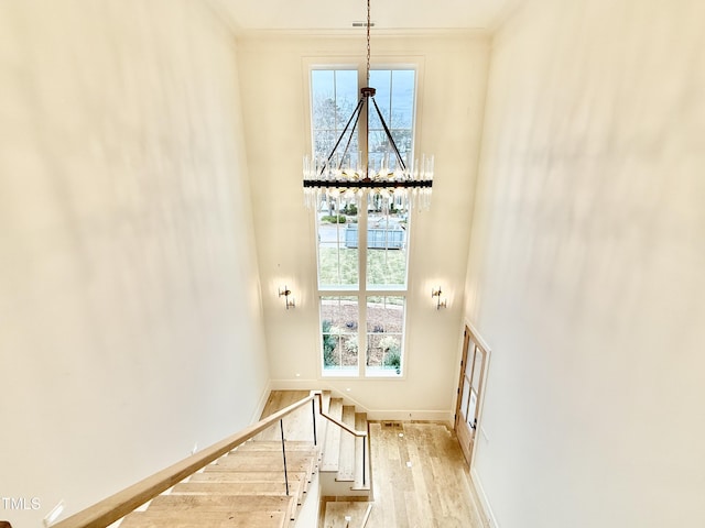 stairs featuring hardwood / wood-style flooring, ornamental molding, a chandelier, and a high ceiling