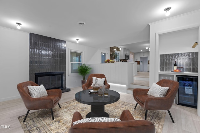 living room featuring a fireplace, light wood-type flooring, crown molding, beverage cooler, and indoor bar