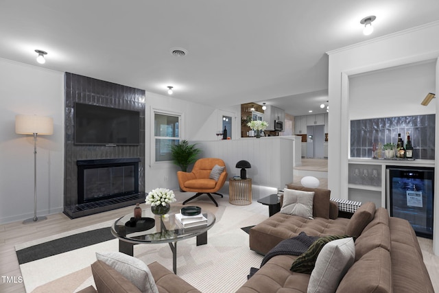 living room featuring a fireplace, crown molding, indoor bar, beverage cooler, and light hardwood / wood-style floors