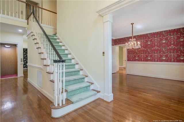 staircase with an inviting chandelier, ornamental molding, and hardwood / wood-style floors