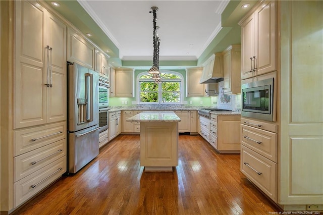 kitchen with appliances with stainless steel finishes, a kitchen island, light stone countertops, light hardwood / wood-style flooring, and decorative light fixtures