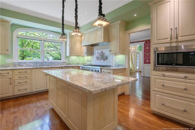 kitchen with light stone counters, stainless steel appliances, a center island, light hardwood / wood-style flooring, and decorative light fixtures