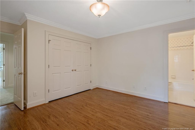 unfurnished bedroom featuring wood-type flooring, crown molding, ensuite bathroom, and a closet