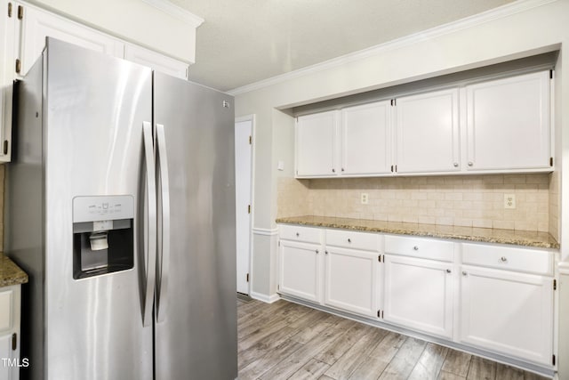 kitchen with stainless steel fridge, white cabinetry, light stone counters, light wood-type flooring, and ornamental molding