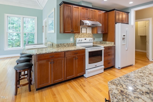 kitchen featuring light wood-type flooring, light stone counters, white appliances, and a kitchen breakfast bar