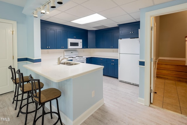 kitchen featuring sink, kitchen peninsula, white appliances, a kitchen breakfast bar, and light wood-type flooring