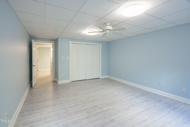 unfurnished bedroom with ceiling fan, light wood-type flooring, a paneled ceiling, and a closet