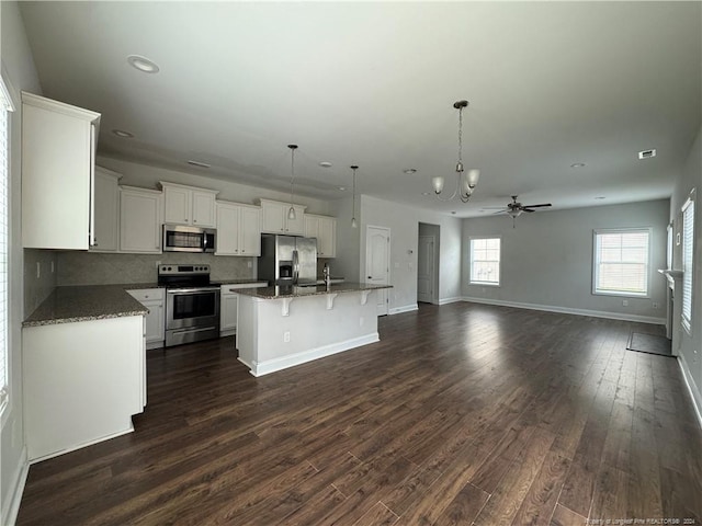 kitchen with stainless steel appliances, dark hardwood / wood-style floors, hanging light fixtures, and a kitchen island with sink