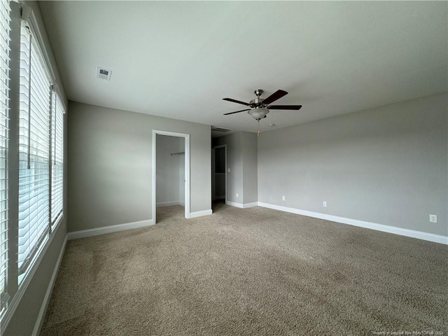 unfurnished bedroom with multiple windows, ceiling fan, a walk in closet, and carpet floors