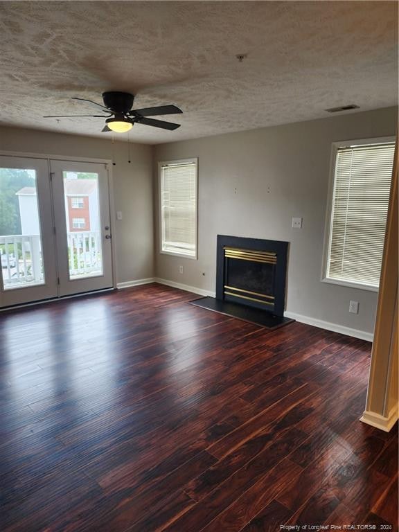 unfurnished living room featuring ceiling fan, dark wood-type flooring, and a textured ceiling