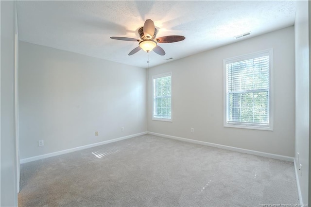 carpeted spare room featuring baseboards, visible vents, and ceiling fan