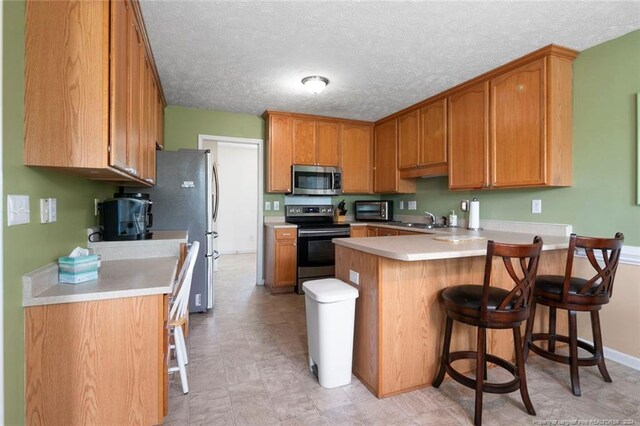 kitchen with a breakfast bar, kitchen peninsula, stainless steel appliances, a textured ceiling, and sink