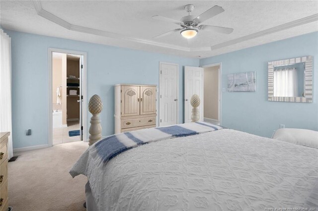 carpeted bedroom with ornamental molding, connected bathroom, a tray ceiling, and ceiling fan