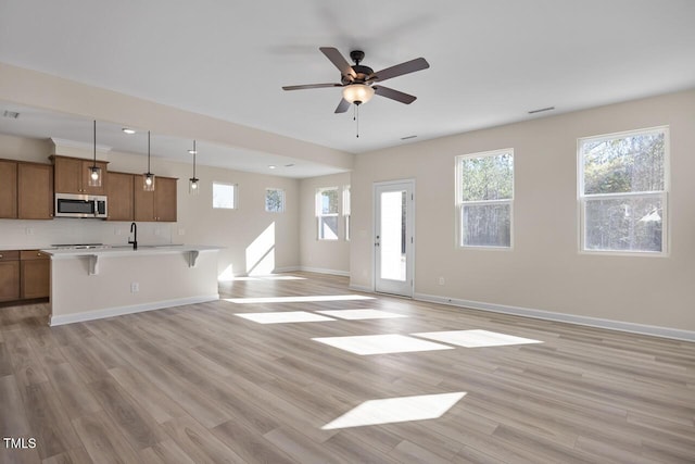 unfurnished living room with sink, ceiling fan, and light hardwood / wood-style flooring