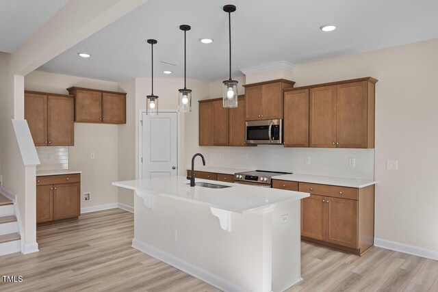 kitchen with light hardwood / wood-style flooring, hanging light fixtures, appliances with stainless steel finishes, sink, and an island with sink