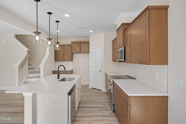 kitchen with hanging light fixtures, a kitchen island with sink, sink, light wood-type flooring, and stainless steel appliances