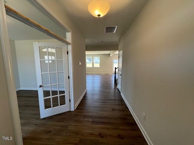 hall featuring dark wood-type flooring, visible vents, and baseboards