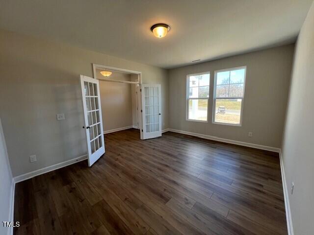 unfurnished bedroom with french doors, dark wood-type flooring, a closet, and baseboards