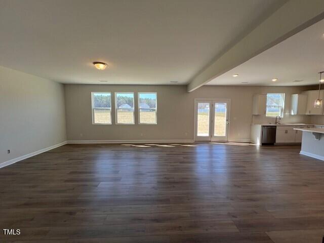 unfurnished living room featuring a sink, dark wood finished floors, beam ceiling, and baseboards