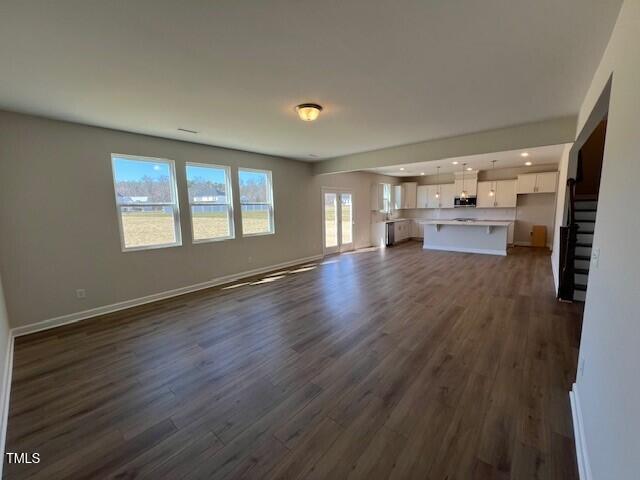 unfurnished living room featuring dark wood-style flooring, stairway, and baseboards