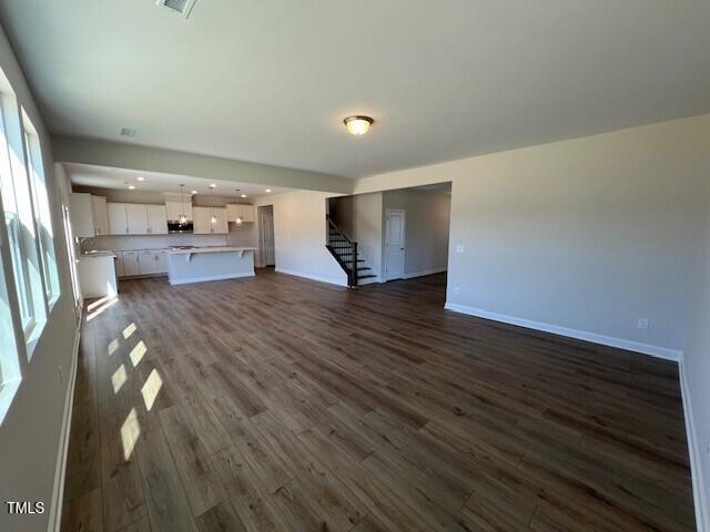 unfurnished living room with baseboards, stairway, dark wood-type flooring, and recessed lighting