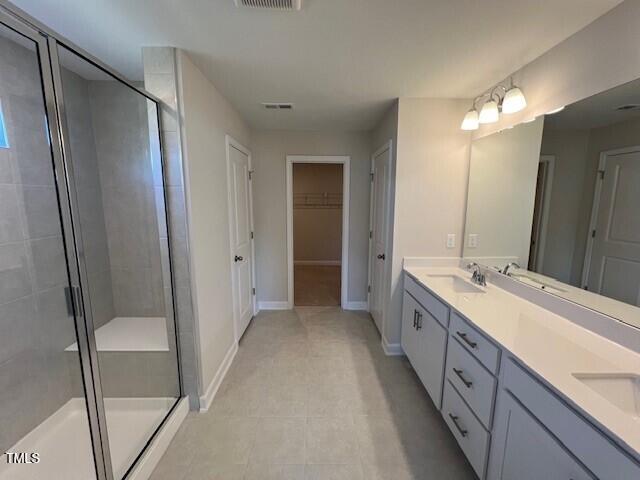 bathroom featuring double vanity, a shower stall, a walk in closet, and a sink