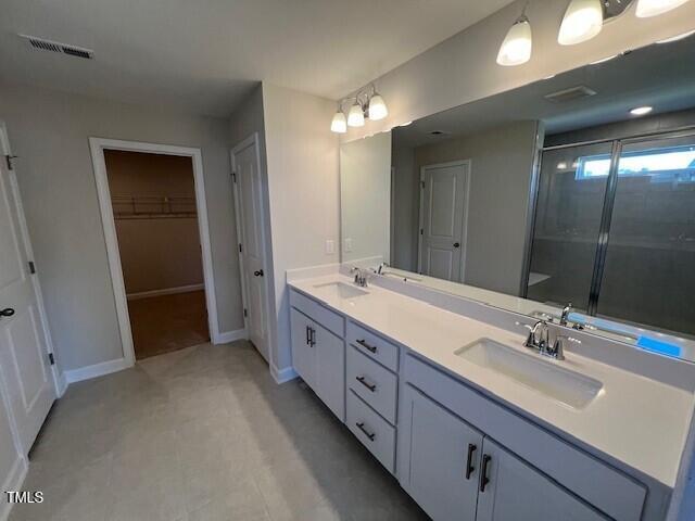 full bath featuring a stall shower, visible vents, a sink, and double vanity