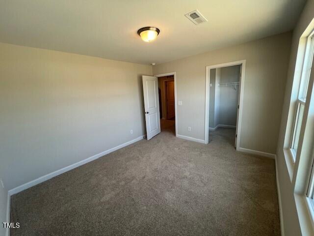 unfurnished bedroom with baseboards, visible vents, carpet, a walk in closet, and a closet