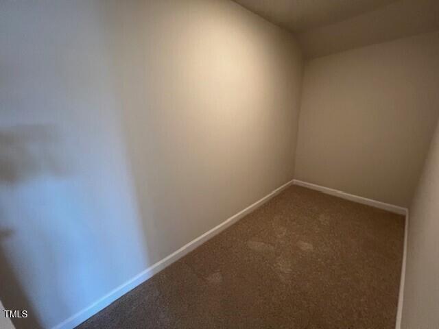 unfurnished room featuring baseboards and dark carpet