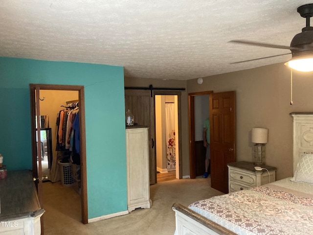 carpeted bedroom with a closet, a textured ceiling, a barn door, a spacious closet, and ceiling fan