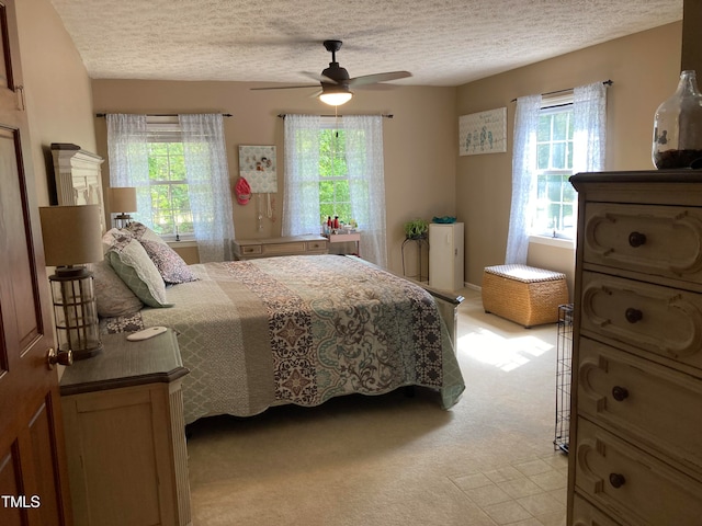 bedroom with ceiling fan, light colored carpet, and a textured ceiling