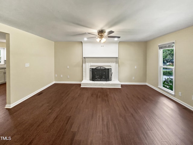 unfurnished living room with ceiling fan, a fireplace, and dark wood-type flooring