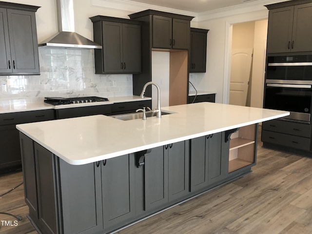 kitchen with stainless steel gas stovetop, sink, ornamental molding, a kitchen island with sink, and wall chimney exhaust hood