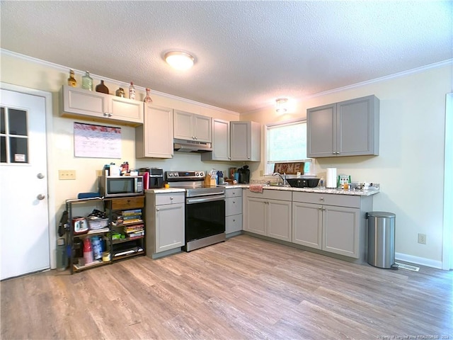 kitchen with light wood-type flooring, a textured ceiling, gray cabinetry, appliances with stainless steel finishes, and crown molding