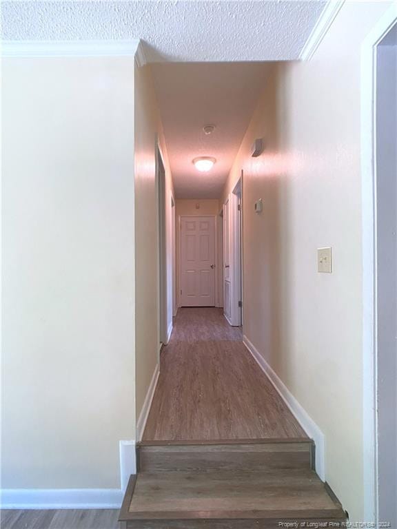 corridor featuring ornamental molding, a textured ceiling, and hardwood / wood-style floors