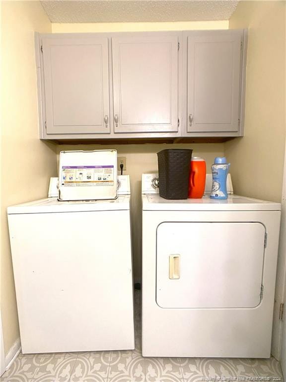 clothes washing area featuring a textured ceiling, washing machine and dryer, and cabinets