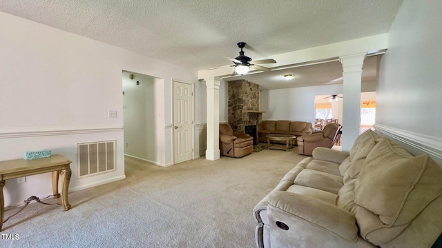 living room featuring ceiling fan, a textured ceiling, light carpet, a fireplace, and ornate columns