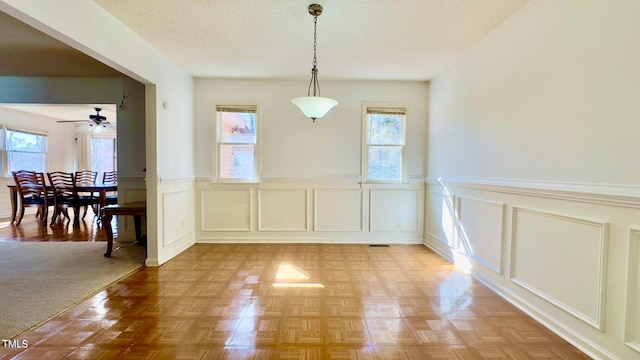 unfurnished dining area with ceiling fan, light colored carpet, and a textured ceiling