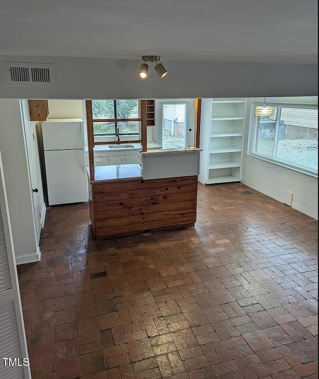 kitchen featuring visible vents, freestanding refrigerator, brick floor, open shelves, and a sink