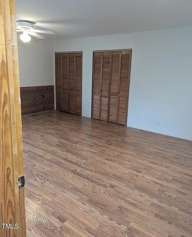 unfurnished bedroom featuring wood finished floors, two closets, and a ceiling fan