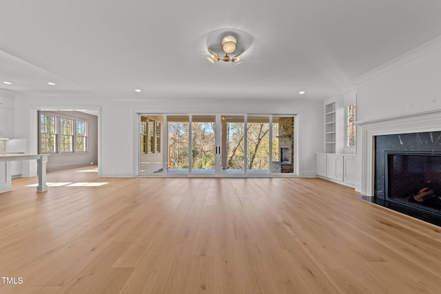 unfurnished living room featuring built in shelves, a high end fireplace, crown molding, and light wood-style flooring