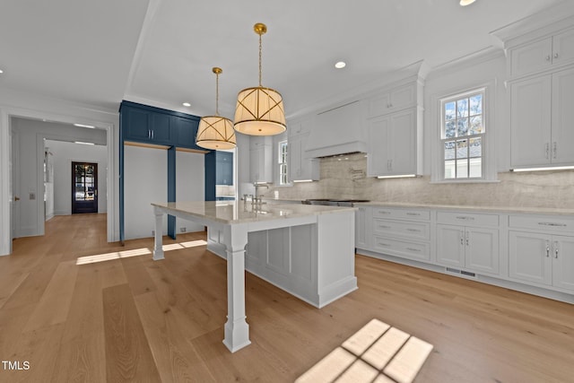 kitchen with a kitchen bar, premium range hood, hanging light fixtures, and light hardwood / wood-style flooring