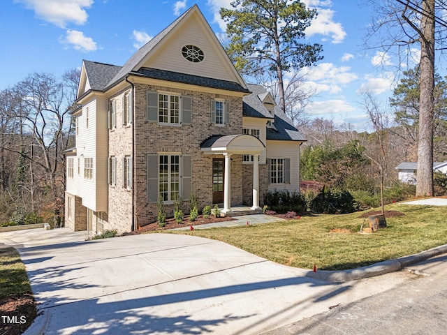 view of front of house featuring brick siding, a shingled roof, concrete driveway, and a front yard