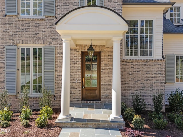 entrance to property featuring brick siding and roof with shingles