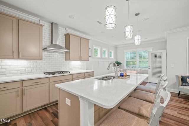 kitchen with stainless steel gas stovetop, an island with sink, sink, hanging light fixtures, and wall chimney exhaust hood