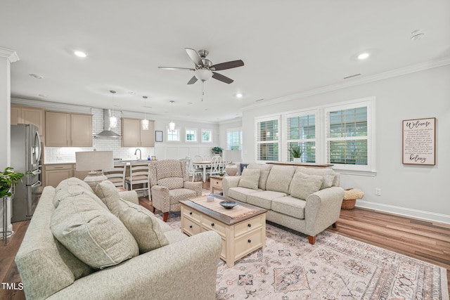 living room with crown molding, ceiling fan, sink, and light wood-type flooring